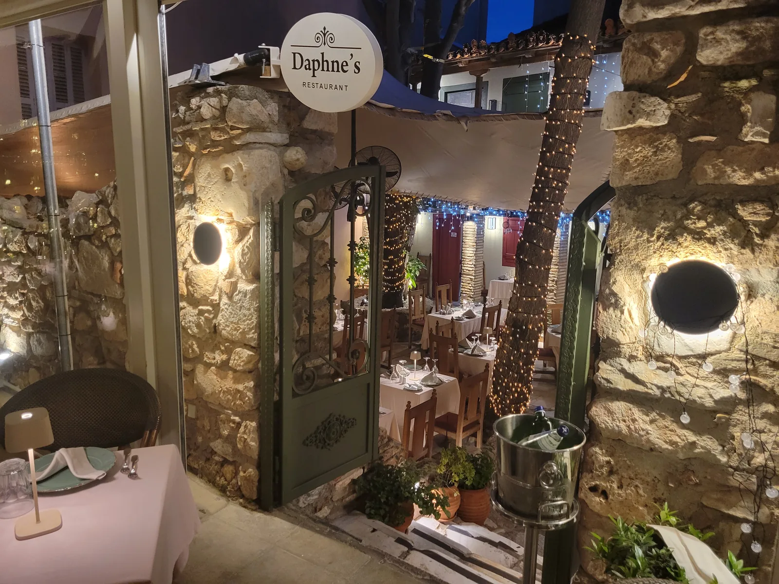Εστιατόριο Daphne's με κήπο — φωτισμός σε πέτρα, φοίνικες με λαμπάκια και τραπέζια με κεριά, Αθήνα